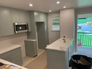 Modern kitchen with gray and white cabinetry, stainless steel appliances, island with waterfall countertop, and recessed lighting