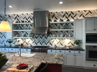 Kitchen with geometric blue and white chevron tile backsplash, gray cabinetry, and granite countertops