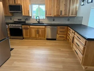 Kitchen with wood cabinetry, stainless steel appliances, hardwood flooring, and tile backsplash