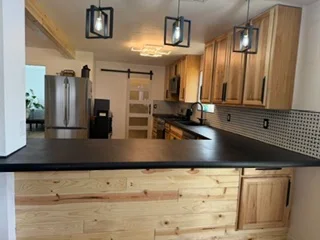 Kitchen with wood cabinets, black countertops, stainless steel appliances, and pendant lights