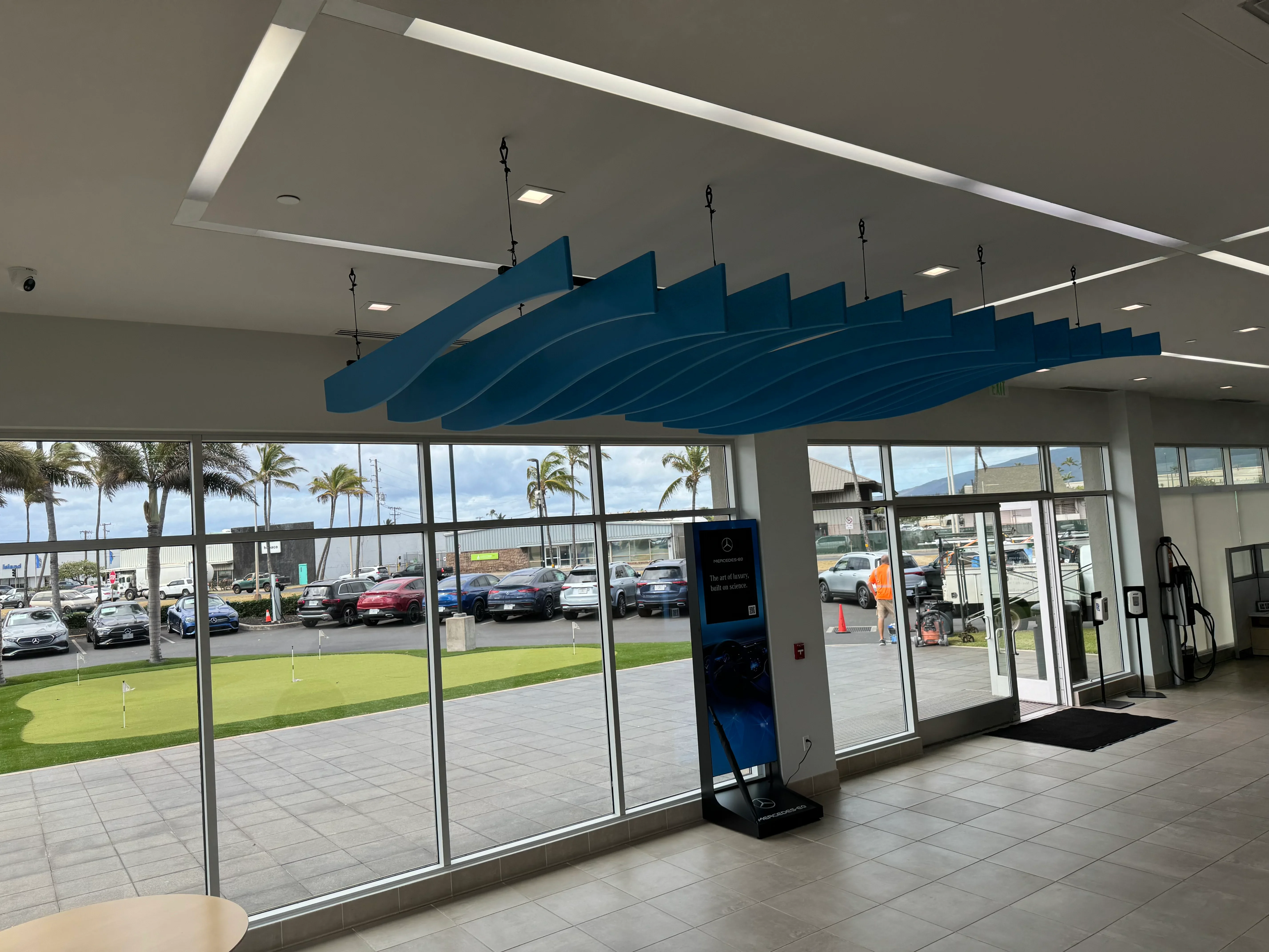 Modern dealership showroom with gray drywall ceiling, blue sculptural feature, recessed lighting, and floor-to-ceiling glass windows