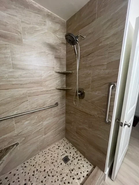 Tiled shower with wood-look porcelain walls, terrazzo floor, rainfall showerhead, and chrome grab bars