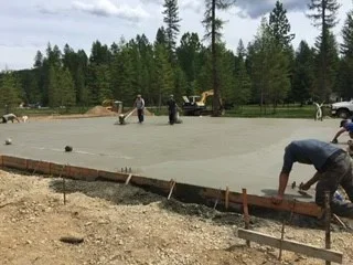 Concrete slab foundation pour with formwork, rebar, and workers on cleared site